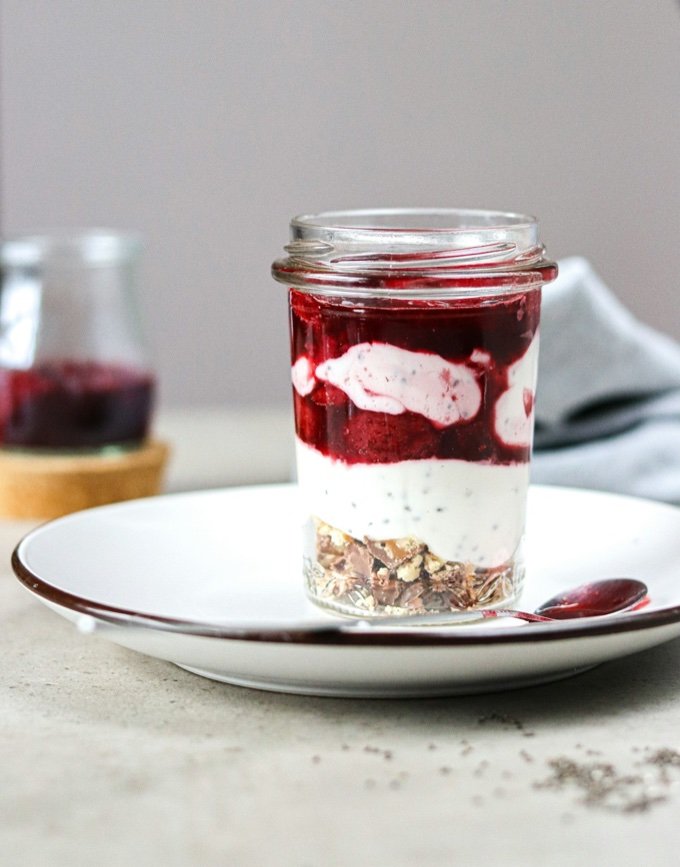 Glas mit laktosefreiem Joghurt mit Beeren auf weißem Teller